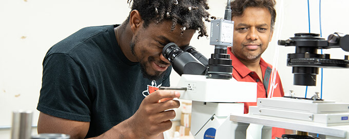 Student looking into a microscope under supervision of lab instructor.